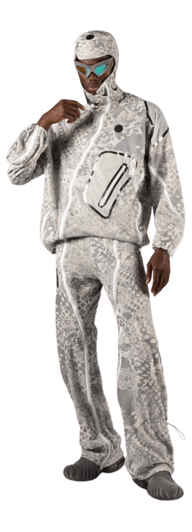 A person adorned in a futuristic outfit features a grey and white patterned hooded jacket crafted from Merino wool, accompanied by matching pants and goggles. The jacket boasts a unique zip design and textured surface, as they stand confidently against a white background.