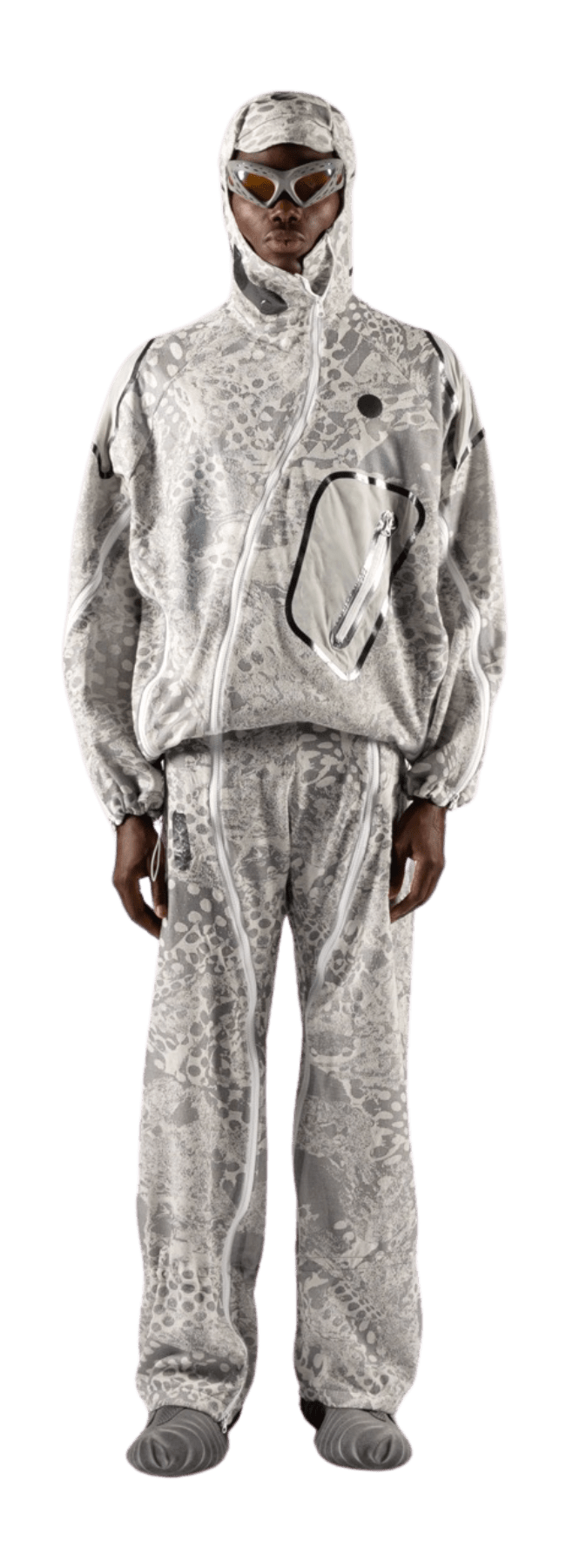 A person donning a matching hooded jacket and pants with a gray snakeskin pattern stands against a plain background. Their outfit, which cleverly incorporates Merino wool, includes an irregularly shaped pocket, while clear protective goggles rest on their forehead.