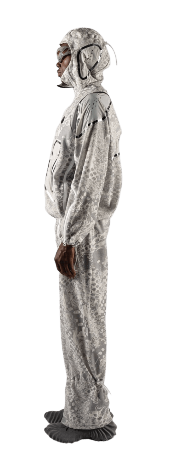 Person in profile wearing a full-body suit resembling a moth, crafted from soft Merino wool. The suit is detailed with a moth-like pattern and includes a headpiece with antennae. The colors are mainly gray and white, giving it an elegant look reminiscent of fine yarn artistry.