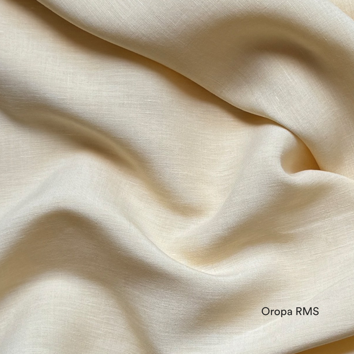 A close-up of smooth, light beige fabric with gentle, flowing folds and a soft texture. The words Oropa RMS are printed in the bottom right corner.