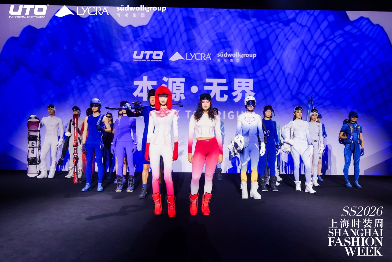 A group of models in futuristic, sporty outfits walk the runway at Shanghai Fashion Week SS2026, with blue and white tones dominating the stage backdrop and clothing styles.