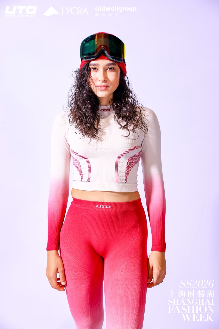 A model wearing a red and white gradient long-sleeve crop top and matching high-waisted leggings poses confidently, with ski goggles on her head, against a light background. Text includes “SHANGHAI FASHION WEEK” and “SS2026”.