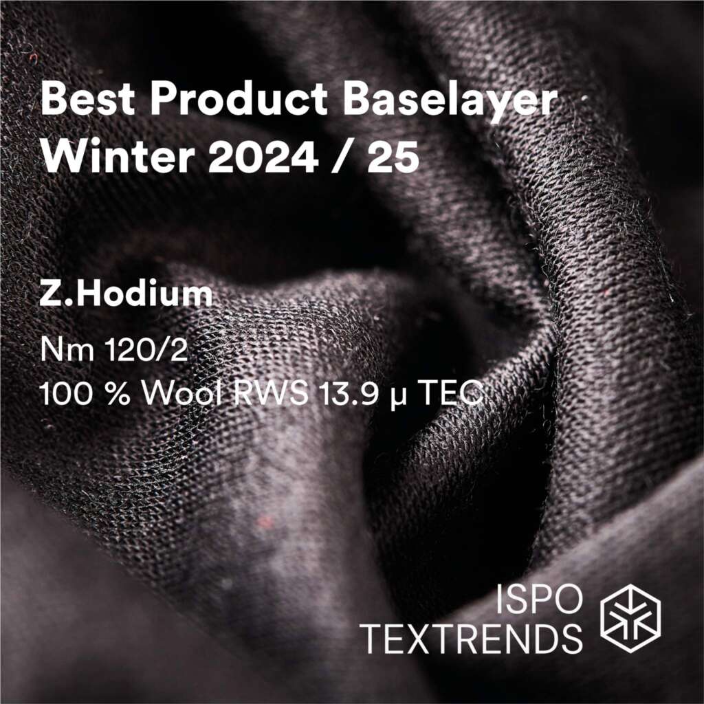 Close-up of textured dark wool fabric with overlaid text: Best Product Baselayer Winter 2024/25, Z.Hodium, Nm 120/2, 100% Wool RWS 13.9 µ TEC, ISPO TEXTRENDS..