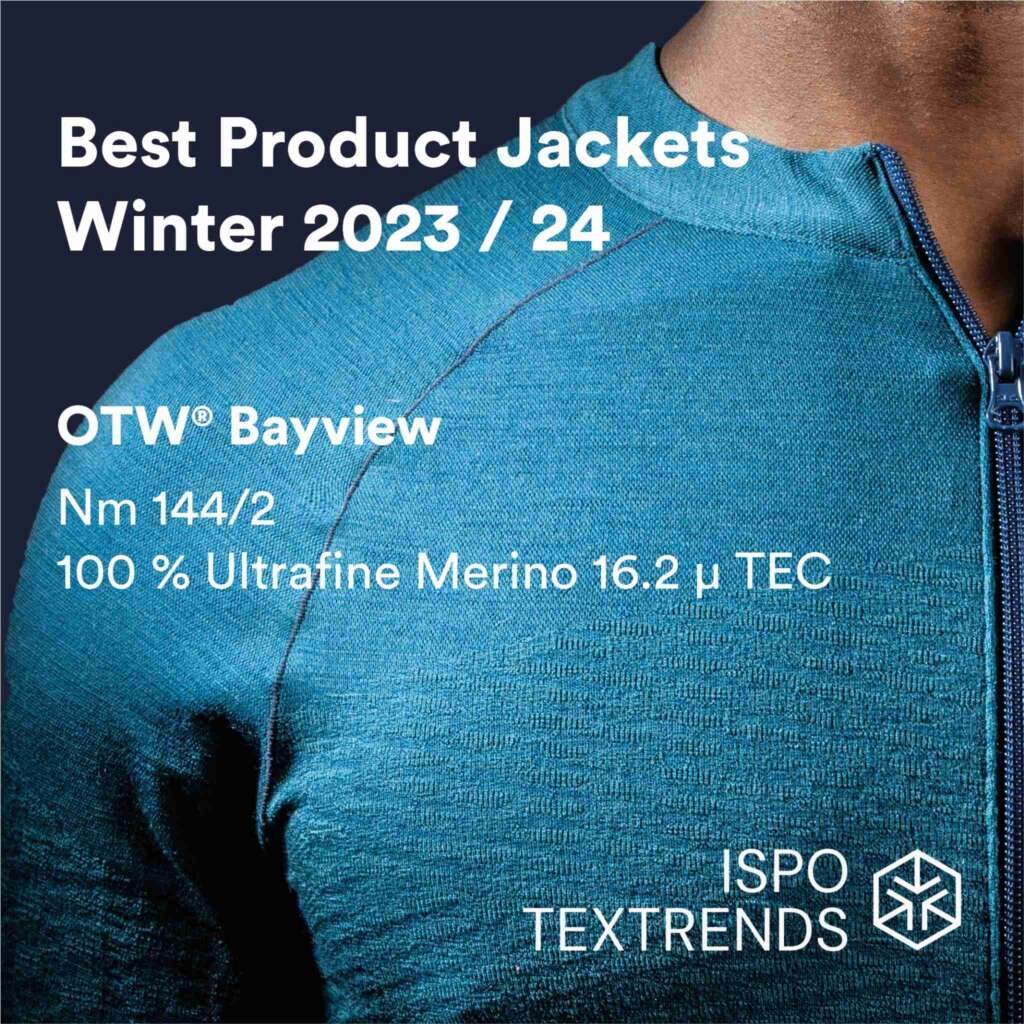 Close-up of a blue merino wool jacket with a zipper, text highlights Best Product Jackets Winter 2023/24, OTW Bayview, ultrafine merino details, and ISPO Textrends logo on the bottom right.