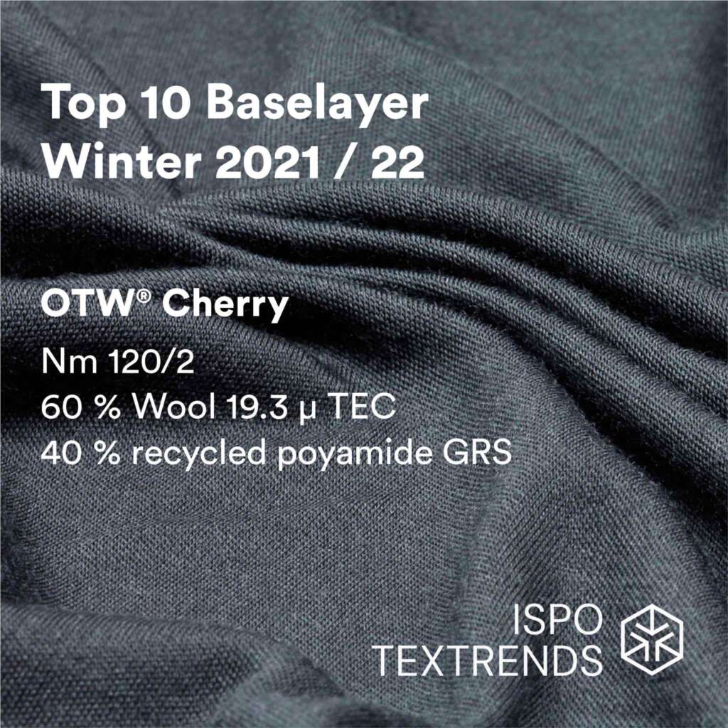 Close-up of dark textured fabric with text: Top 10 Baselayer Winter 2021/22. OTW® Cherry. Nm 120/2. 60% Wool 19.3 μ TEC. 40% recycled polyamide GRS. ISPO TEXTRENDS logo in corner.
