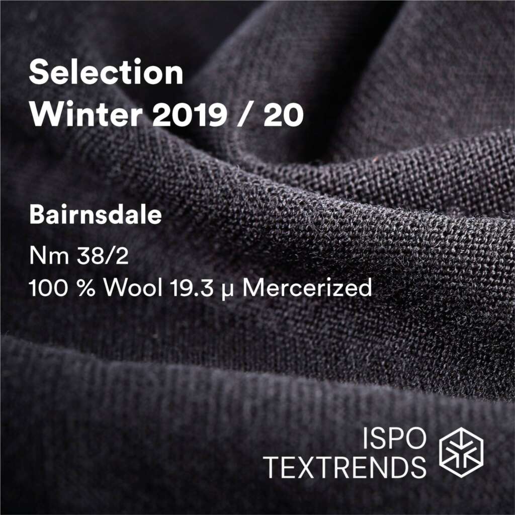 Close-up of dark textured wool fabric with text: Selection Winter 2019/20, Bairnsdale, Nm 38/2, 100% Wool 19.3 μ Mercerized, ISPO TEXTRENDS in white over the fabric.